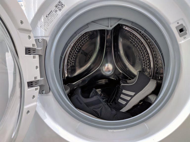 Close-up of black sneakers inside a washing machine drum showcasing laundry theme.